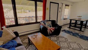 A room with a sofa, a wooden table, a patterned rug, and a view through large windows. - Kelli's Harbor Suites - In Auke Bay Walking Community - DISCOUNT ON TOURS (Juneau)