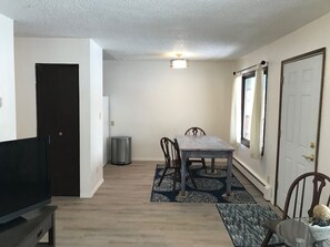 A dining area with a table and chairs, a trash can, and a ceiling light fixture. - Kelli's Harbor Suites - In Auke Bay Walking Community - DISCOUNT ON TOURS (Juneau)
