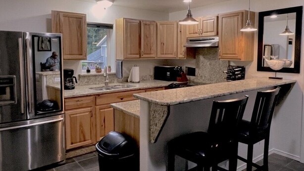 A modern kitchen with wooden cabinets, stainless steel appliances, a granite countertop, and bar stools.