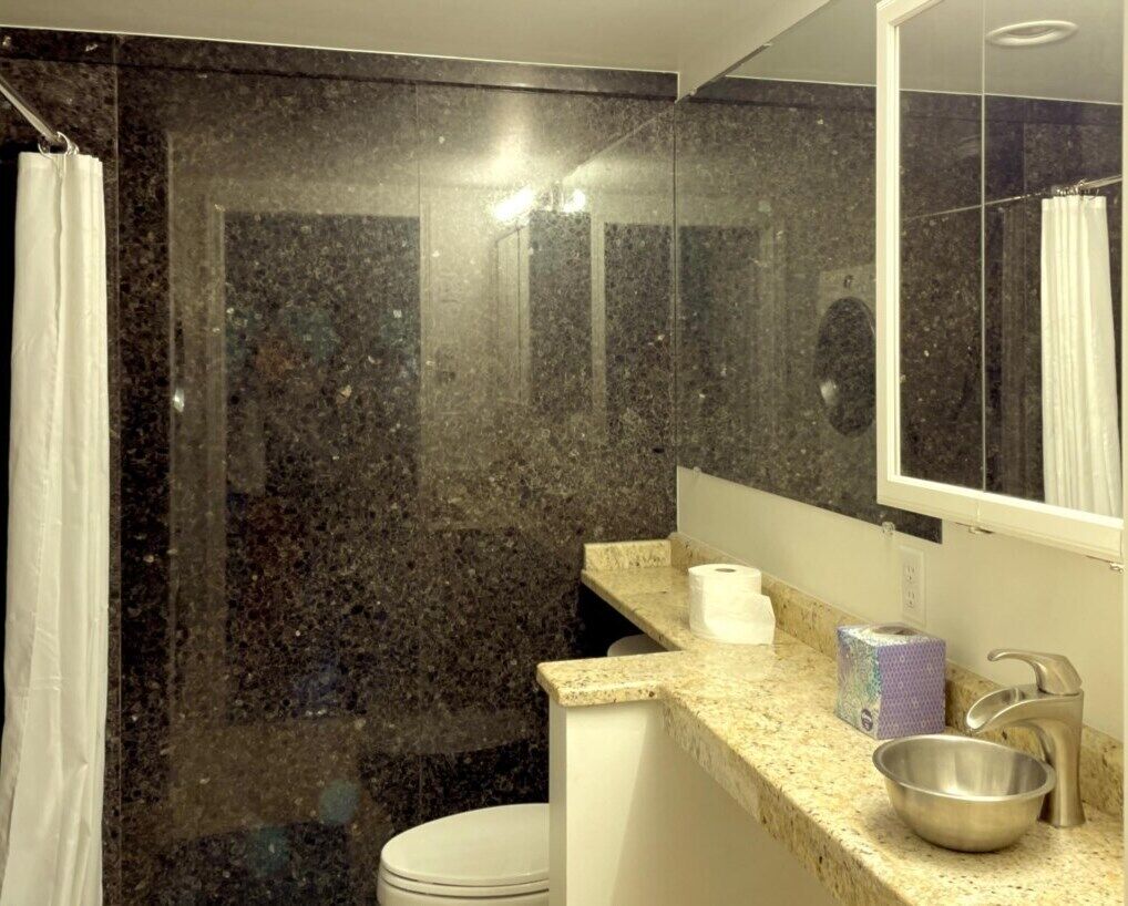 Une salle de bain avec un comptoir en granit, un lavabo, un miroir et un rideau de douche.