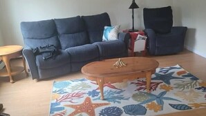 A living room with a blue sofa, a wooden coffee table, and a colorful rug with sea-themed designs. - Rainbow Row - Three Private Units in Complex, near Mendenhall Glacier, Trails, and Conveniences! (Juneau)