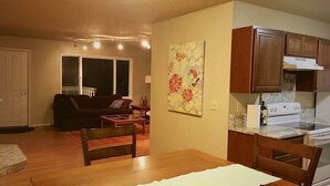 A living room with a couch, a dining table, and a kitchen area with cabinets and a stove. - Rainbow Row - Three Private Units in Complex, near Mendenhall Glacier, Trails, and Conveniences! (Juneau)