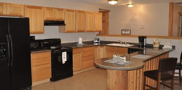 A kitchen with wooden cabinets, a black refrigerator, a stove, and a sink. - Cozy Wisconsin home a block off Lake Arbutus. (Merrillan)