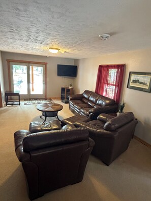 A living room with a sectional sofa, a coffee table, a flat-screen TV, and a door leading outside.