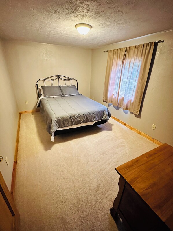 A bedroom with a bed, a wooden dresser, a window with curtains, and a ceiling light. - Cozy Wisconsin home a block off Lake Arbutus. (Merrillan)