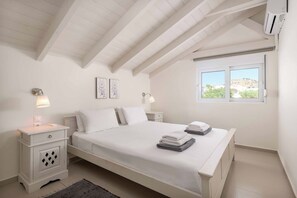Un dormitorio con cama, mesitas de noche, lámparas de pared, una ventana con vistas y un techo con vigas a la vista.