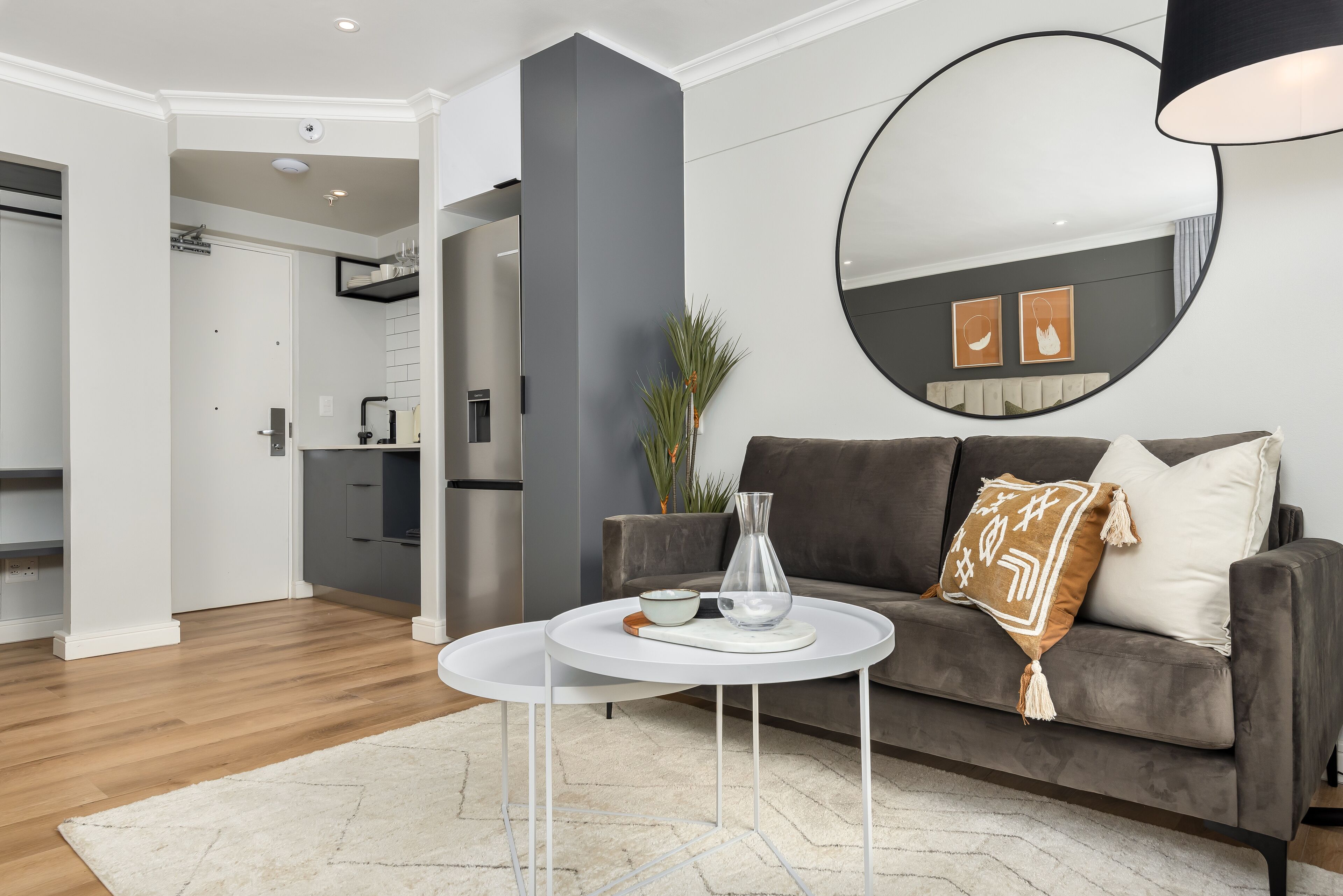 A modern living room with a grey sofa, a white coffee table, and a large round mirror on the wall.