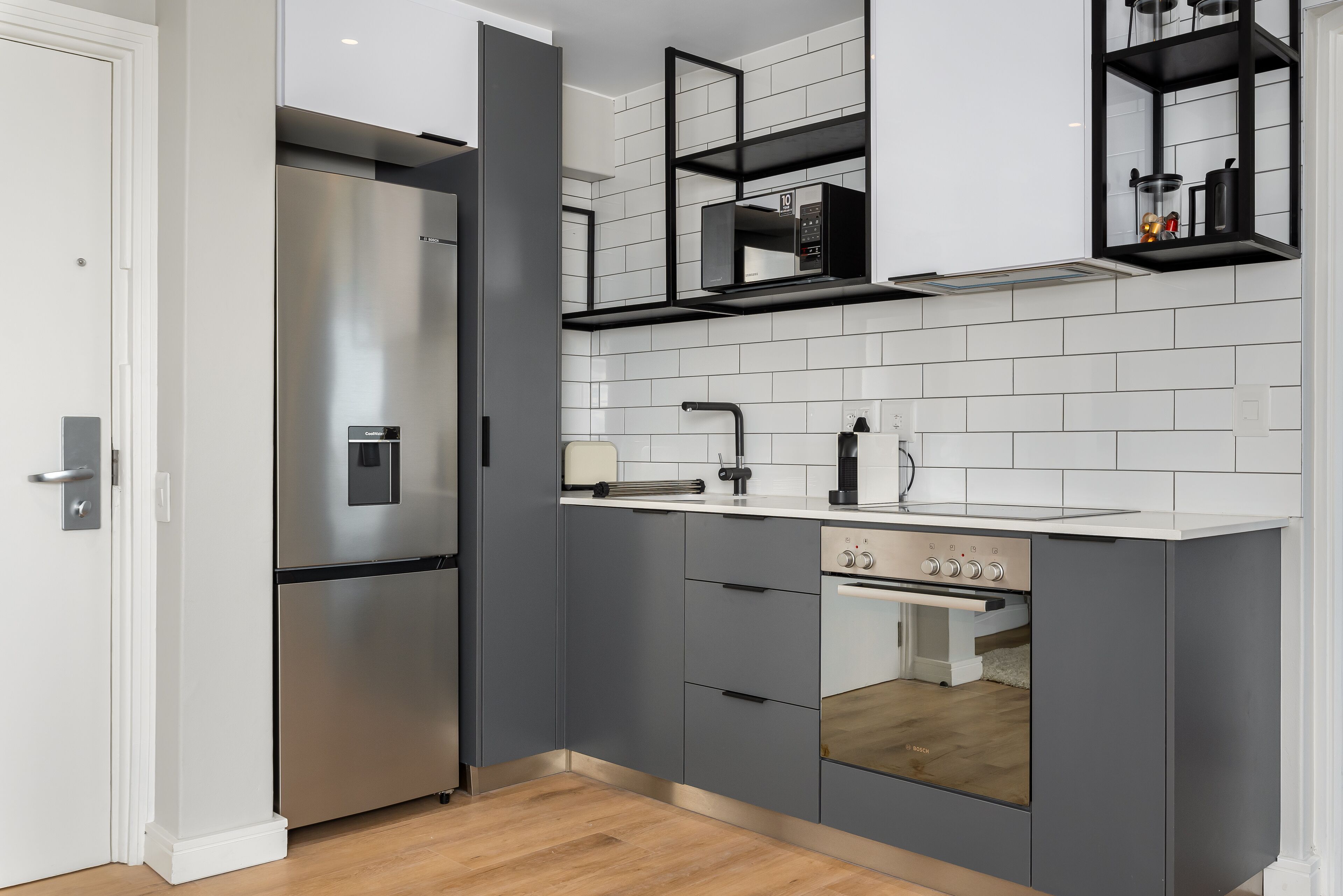 Une cuisine moderne avec des meubles gris, un réfrigérateur en acier inoxydable, un four Bosch et un dosseret de carrelage blanc.