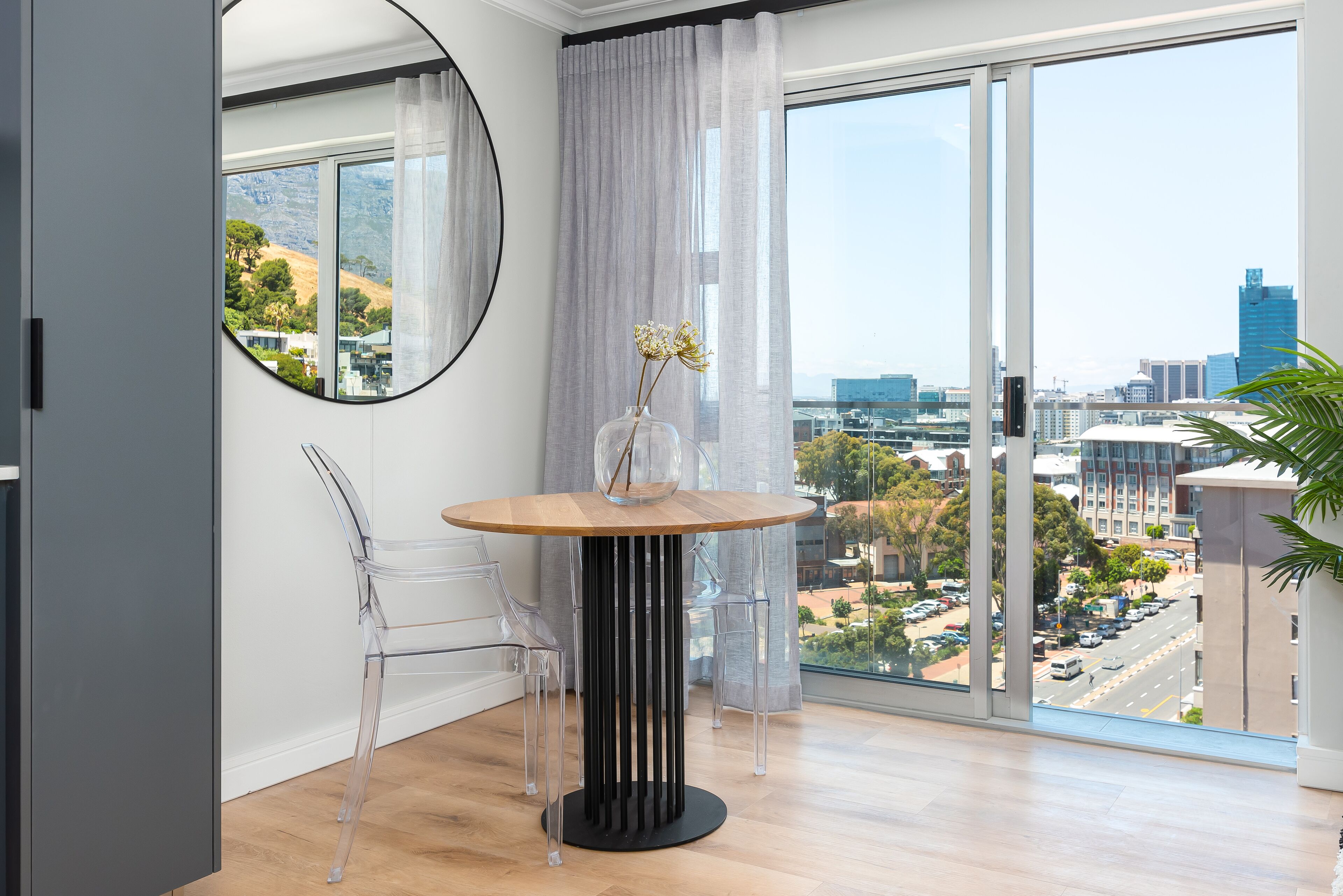 A modern room with a large window, a round table with a vase, and clear chairs.