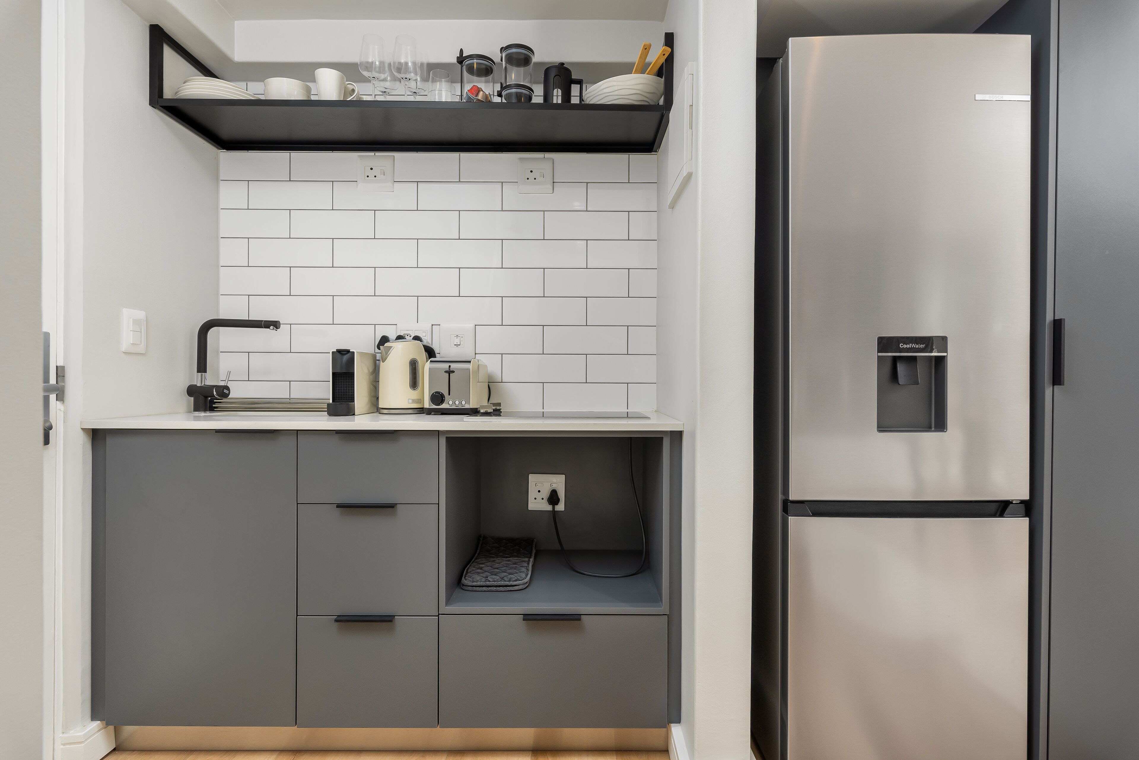 A compact kitchen with a built-in refrigerator, a countertop with a coffee maker, and a shelf above the sink.