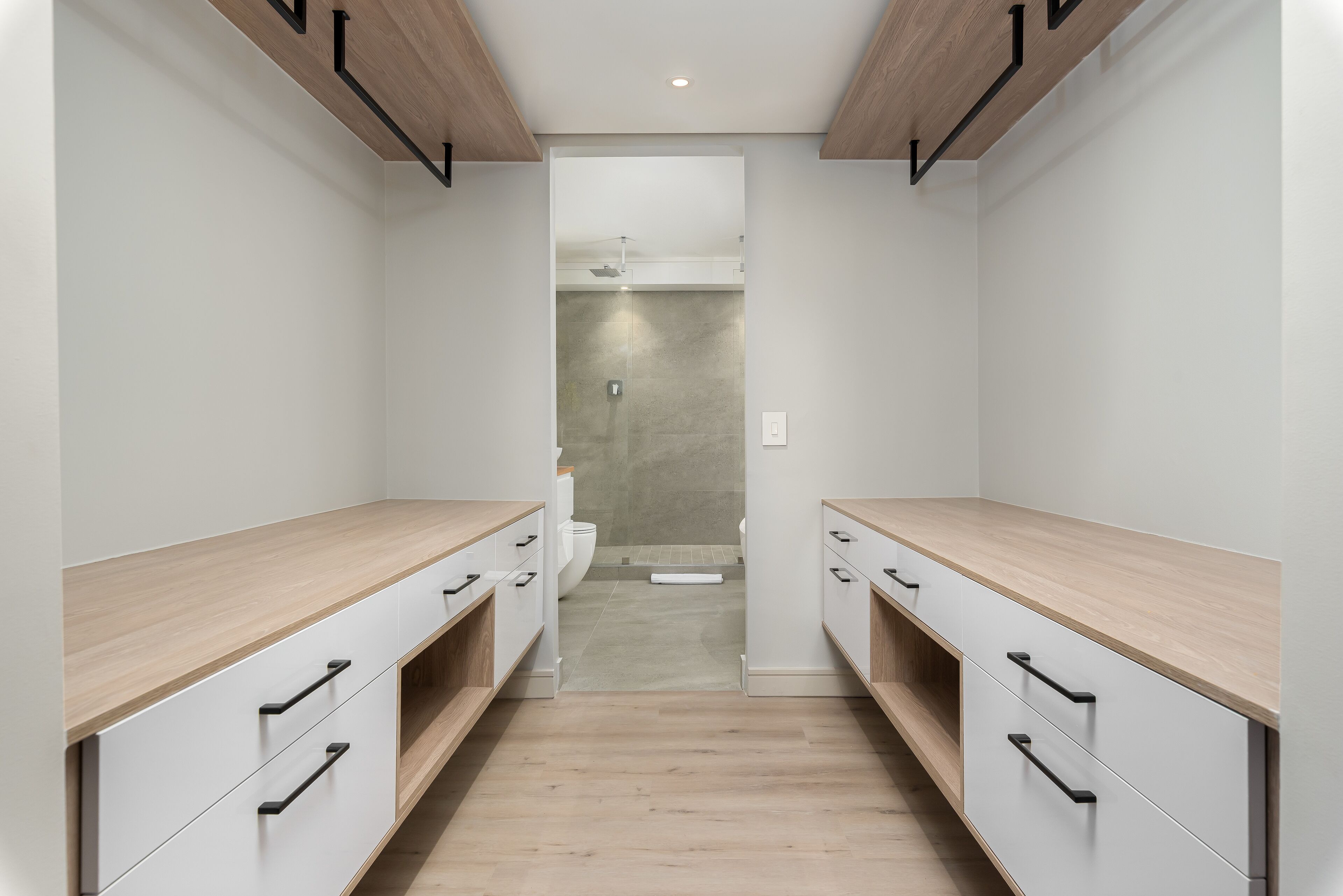 Ein schmaler Flur mit Holzboden, weißen Wänden und einer Spiegeltür zu einem Badezimmer mit Dusche und Toilette.