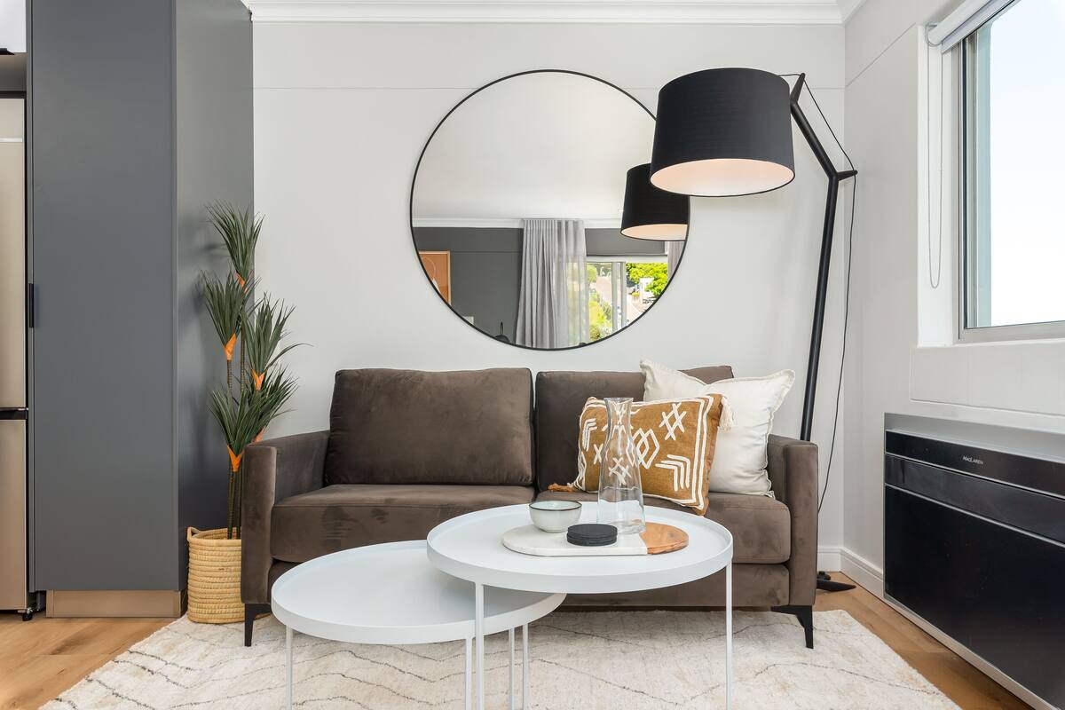 A modern living room with a grey sofa, a round mirror, a white coffee table, and a floor lamp.