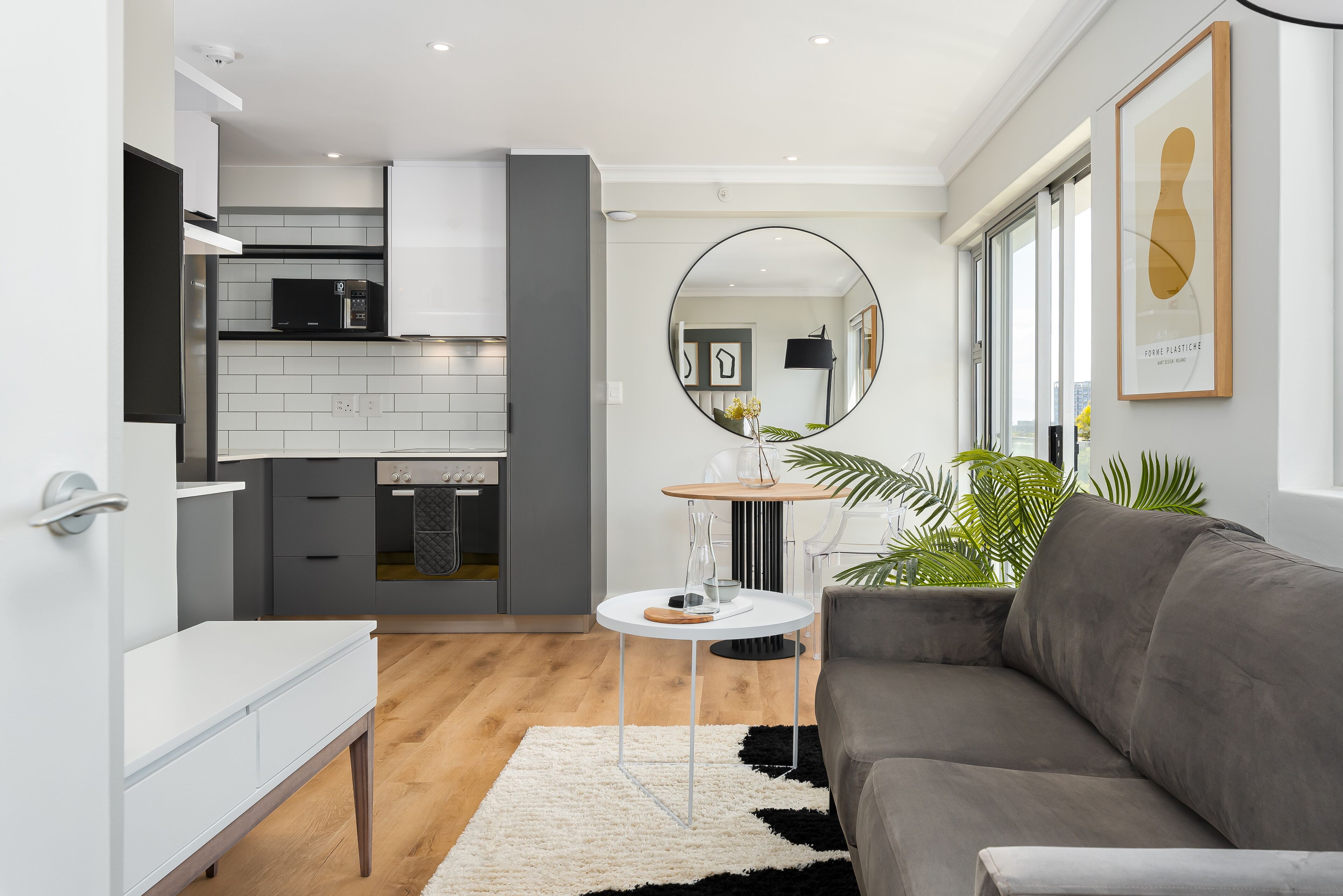 A modern kitchen with white cabinets, a black microwave, and a round table with a glass top.