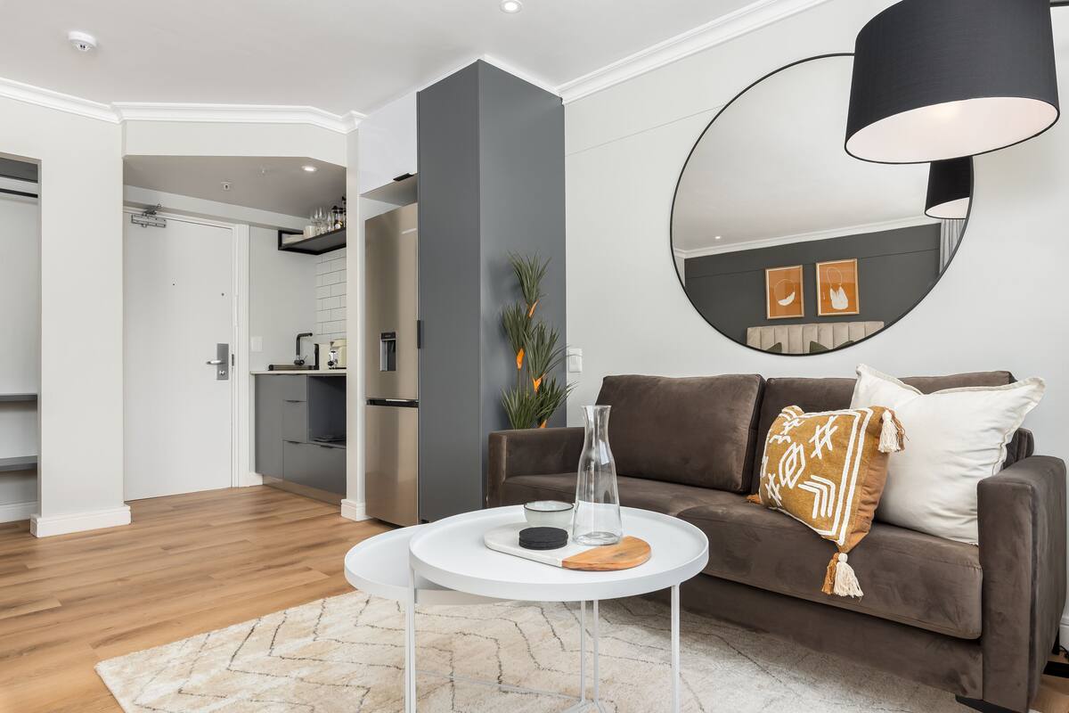 A modern living room with a brown sofa, a white coffee table, and a large mirror.