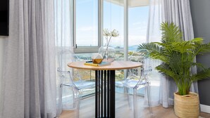 A modern room with a round table, clear chairs, a potted plant, and a view through large windows.