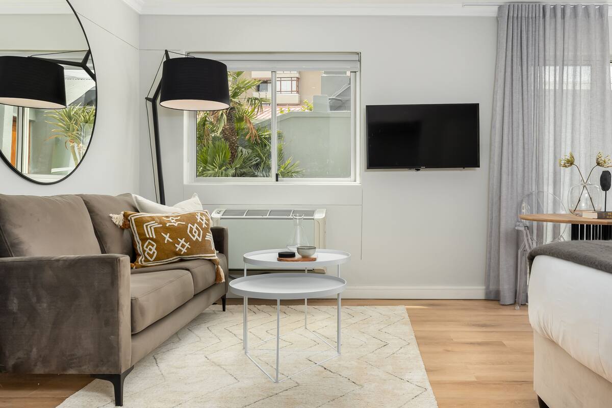 A modern living room with a sofa, a coffee table, a TV, and a window with a view of greenery.