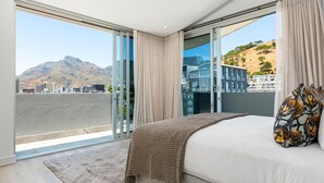 A bedroom with a large bed, a view of a cityscape, and a mountain in the background.