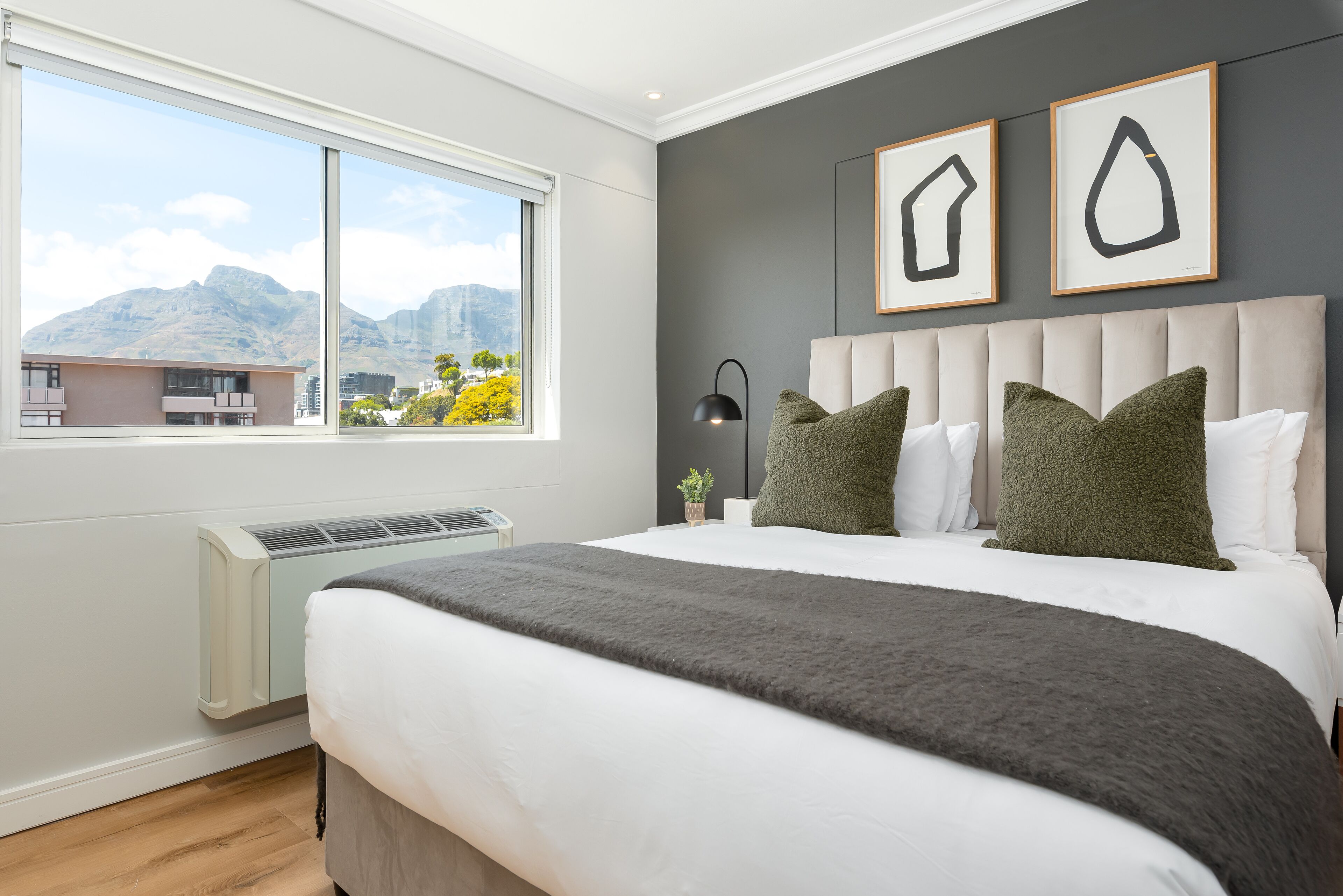 Un dormitorio moderno con una cama grande, vistas a las montañas y dos cuadros abstractos en la pared.