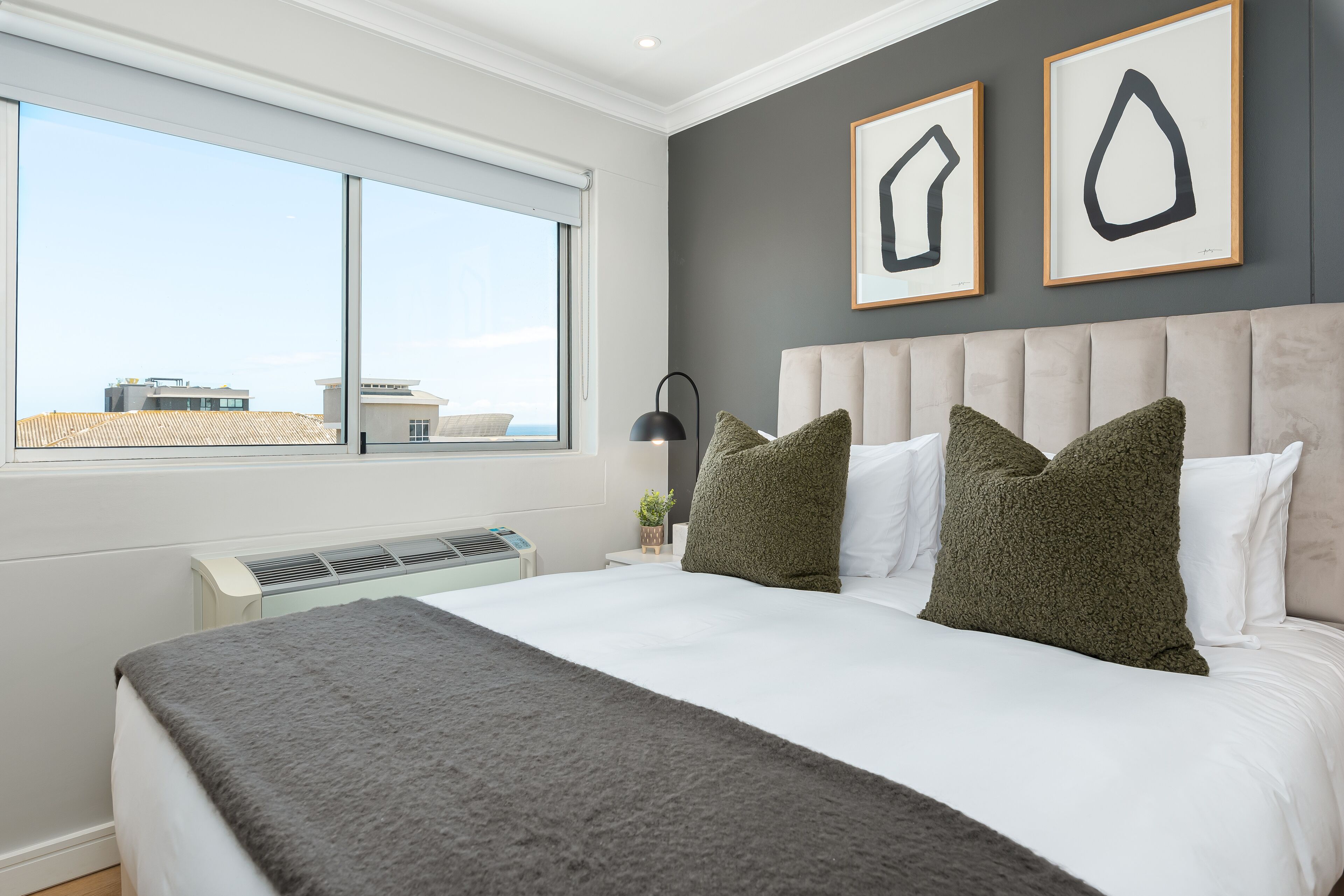 Une chambre avec un grand lit, une fenêtre et deux œuvres d’art encadrées accrochées au mur.