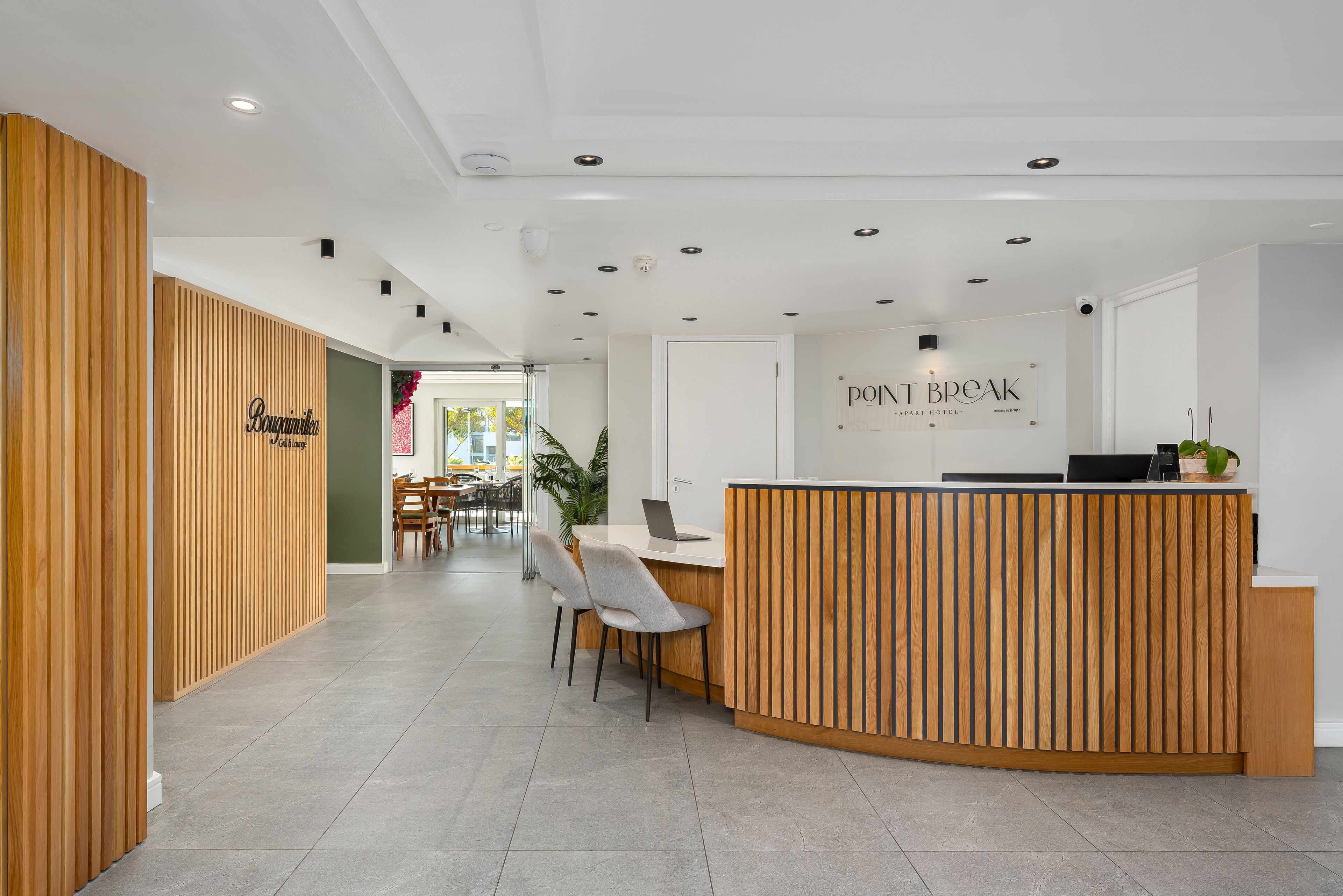 A hotel reception area with a wooden reception desk, a seating area with chairs, and a view into the dining space.