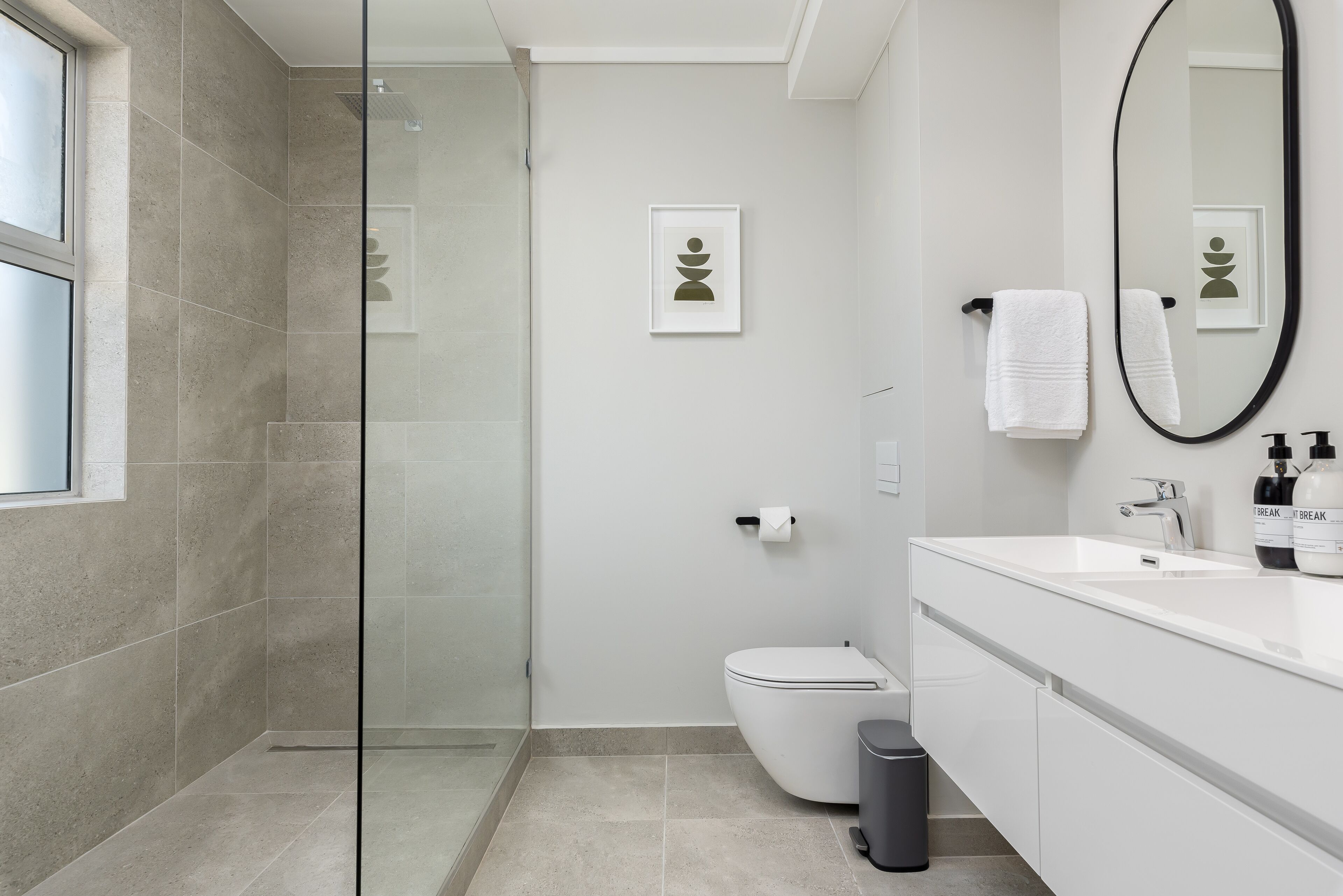 Un baño moderno con cabina de ducha de vidrio, inodoro y tocador blanco con espejo y dos botellas de jabón de manos.