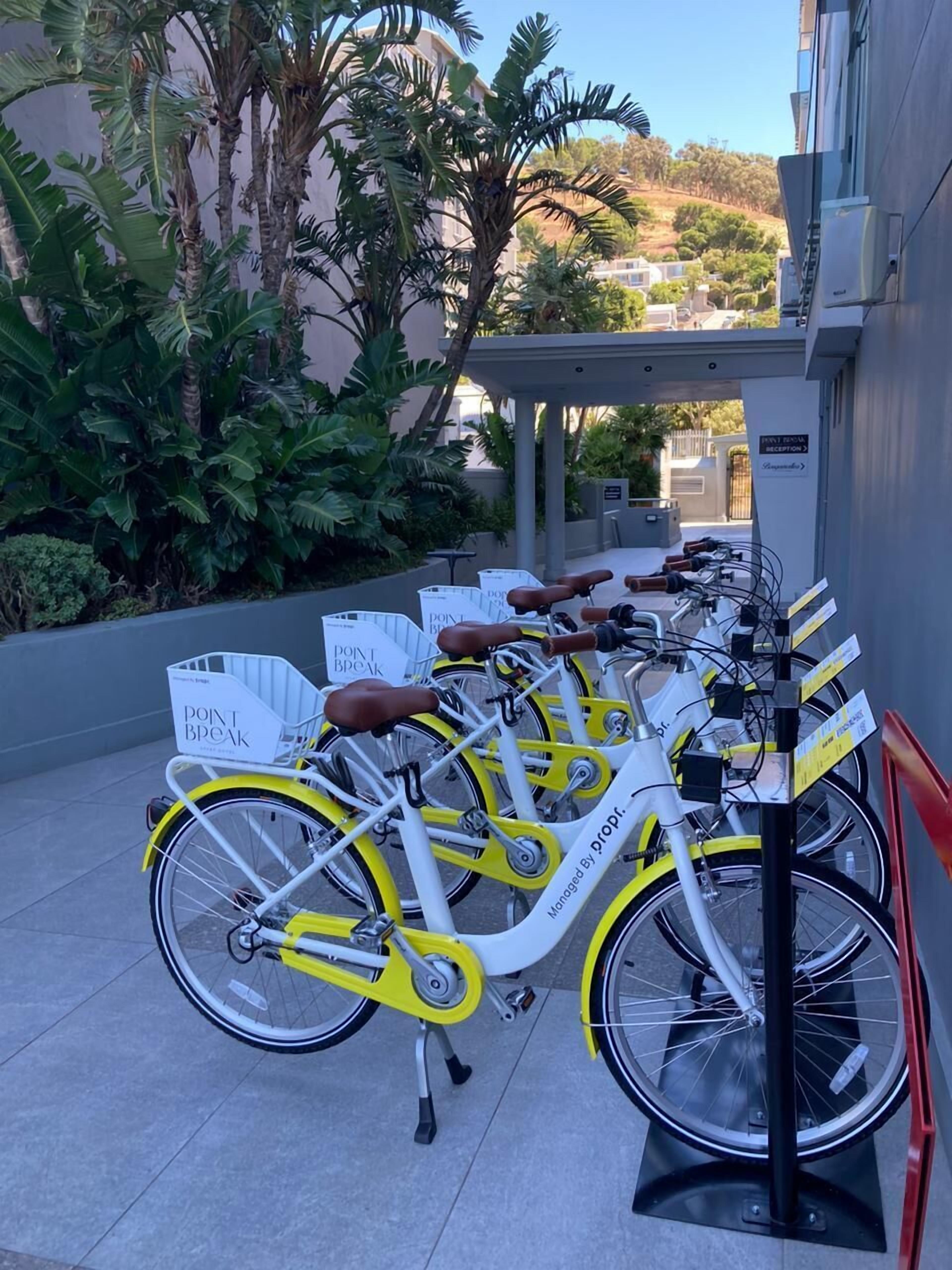 Una fila di biciclette bianche e gialle parcheggiate in un'area esterna, con un cartello che segnala una zona di surf.