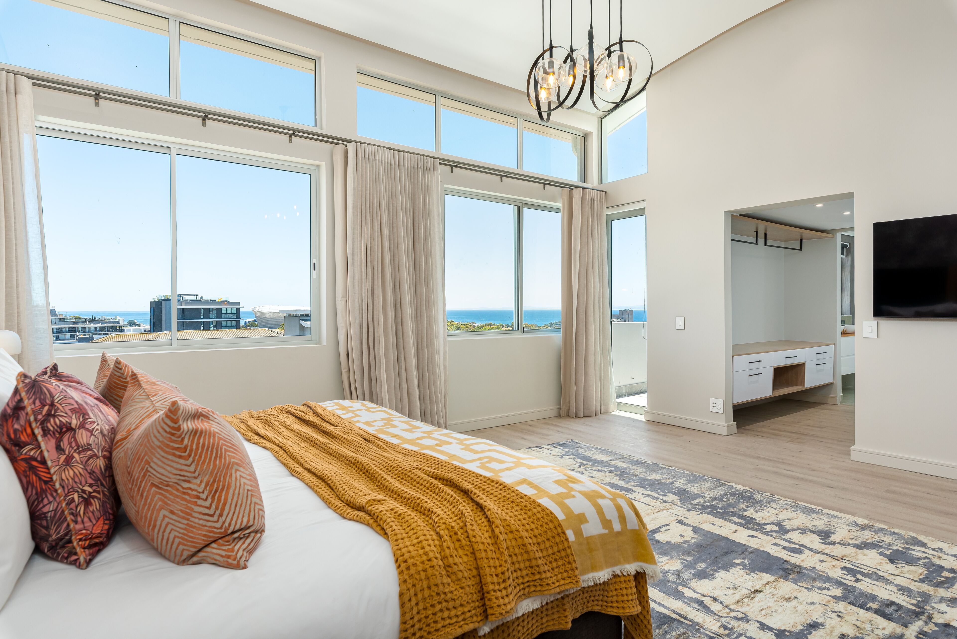 A bedroom with a large bed, a view of the sea, and a TV mounted on the wall.
