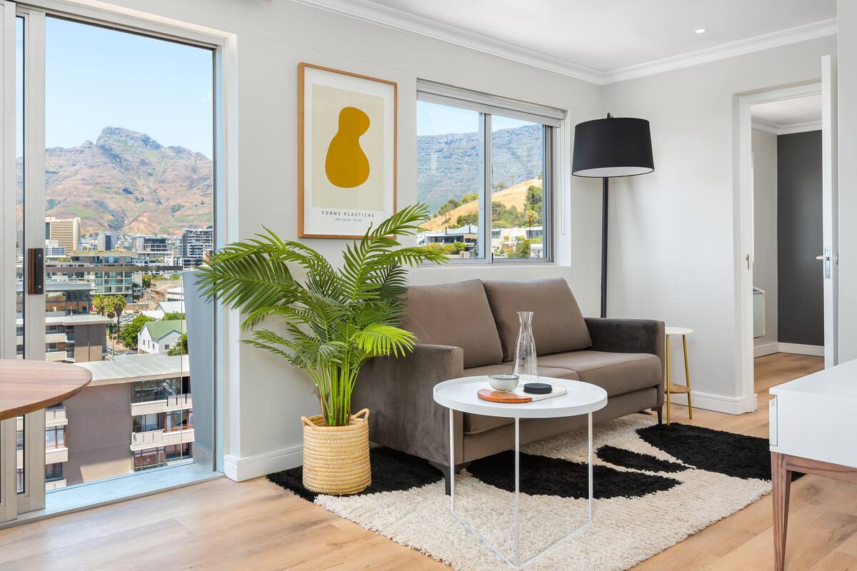 A modern living room with a large window, a sofa, a coffee table, and a potted plant.