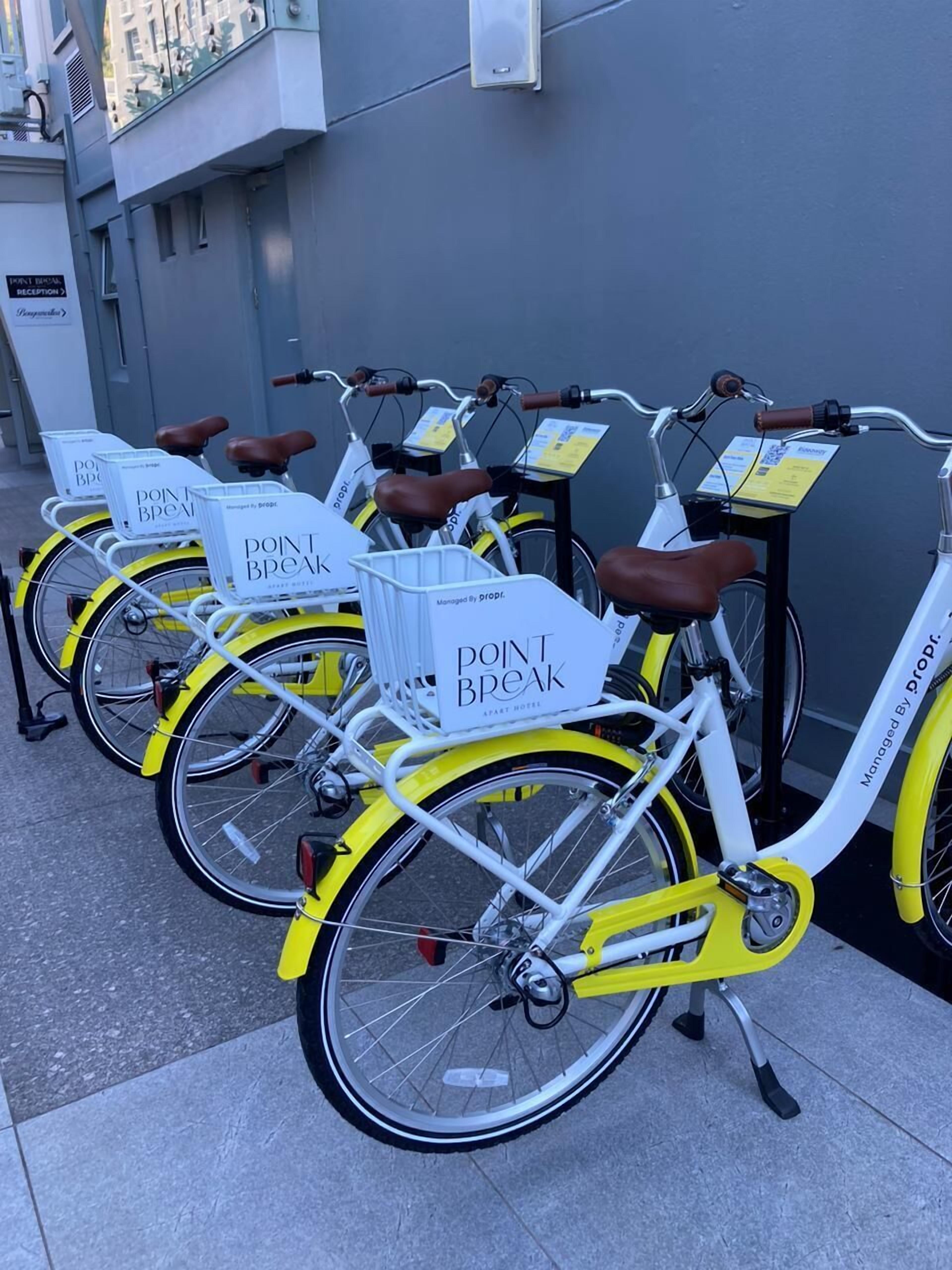 A row of bicycles with baskets labeled "POINT BREAK" parked against a building.