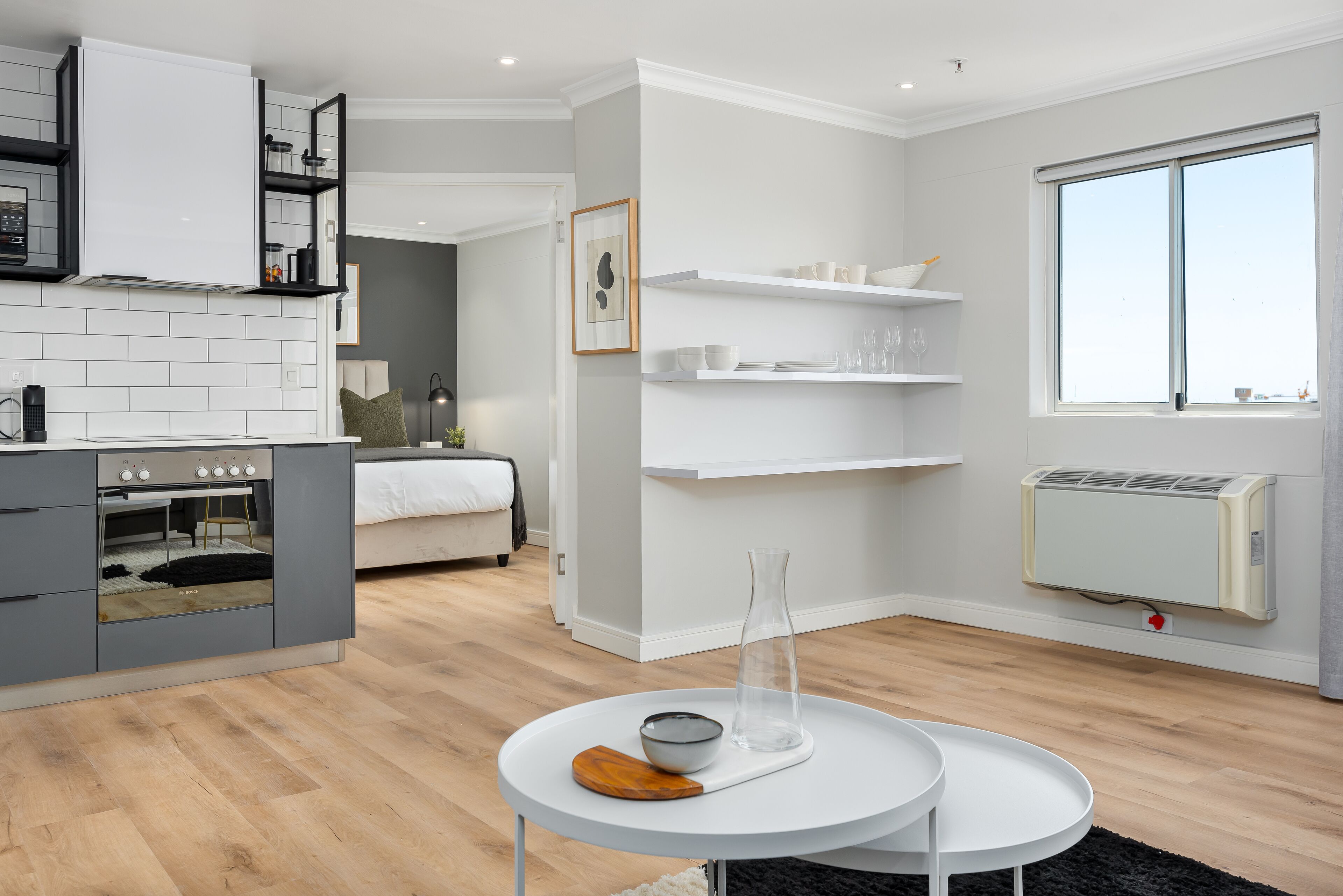 A modern kitchen with white cabinets, a built-in oven, and a dining area with a round table and a vase.