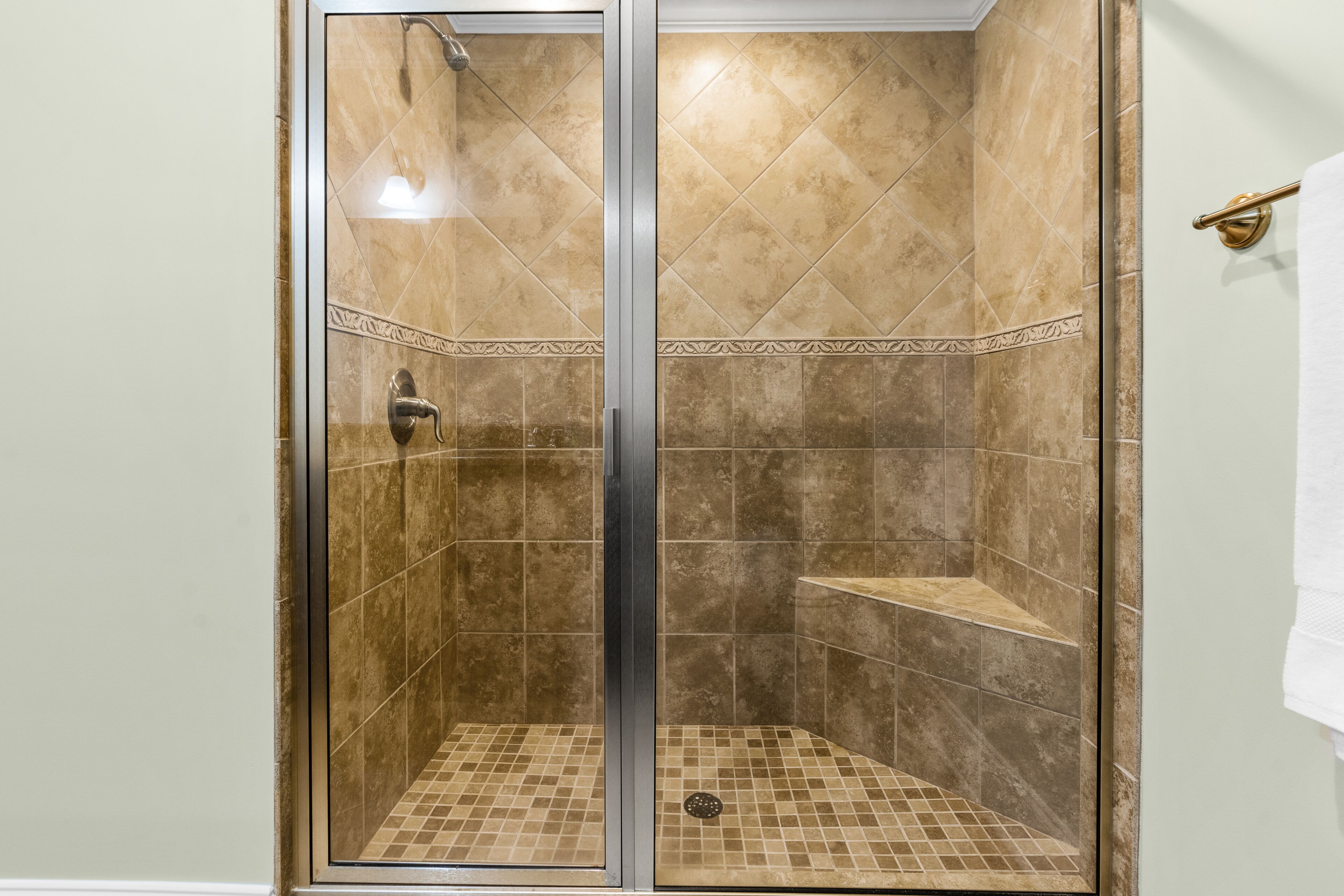 A glass-enclosed shower with beige tiles and a metal door.