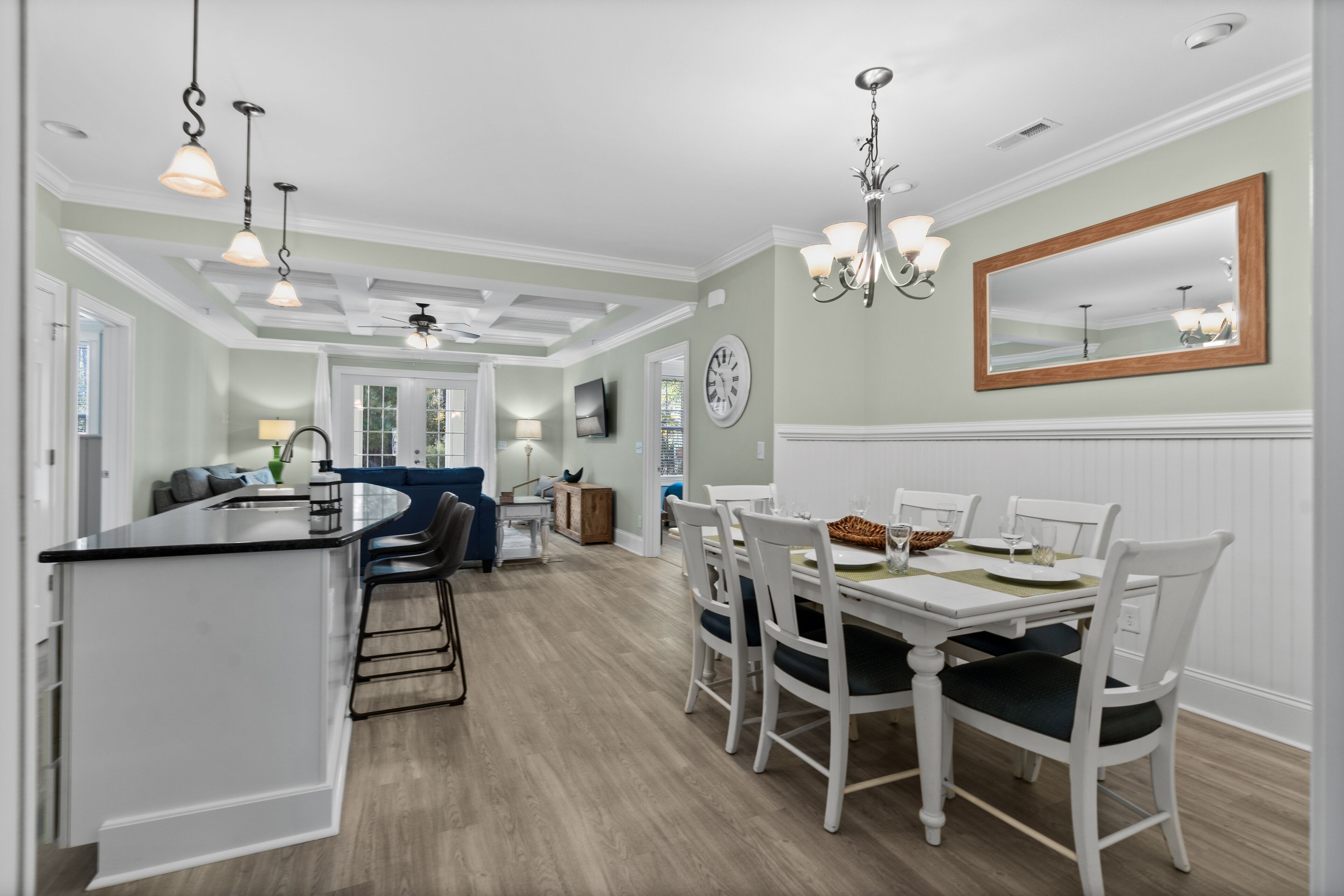 A modern kitchen with a central island, dining area with white chairs, and a large mirror on the wall.