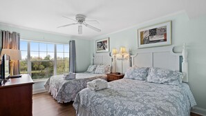 A hotel room with two beds, a desk, a ceiling fan, and large windows offering a view of the outdoors. - Beach Vibes 1BR Condo in Litchfield (Pawleys Island)