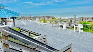 A wooden boardwalk with white chairs and tables, overlooking a beach and the ocean. - Beach Vibes 1BR Condo in Litchfield (Pawleys Island)