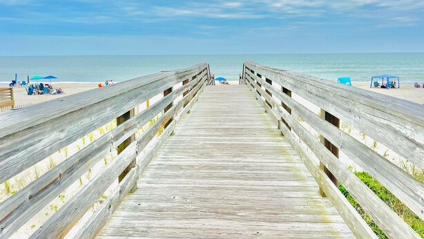 A wooden boardwalk leading to a beach with umbrellas and beach chairs. - Beach Vibes 1BR Condo in Litchfield (Pawleys Island)