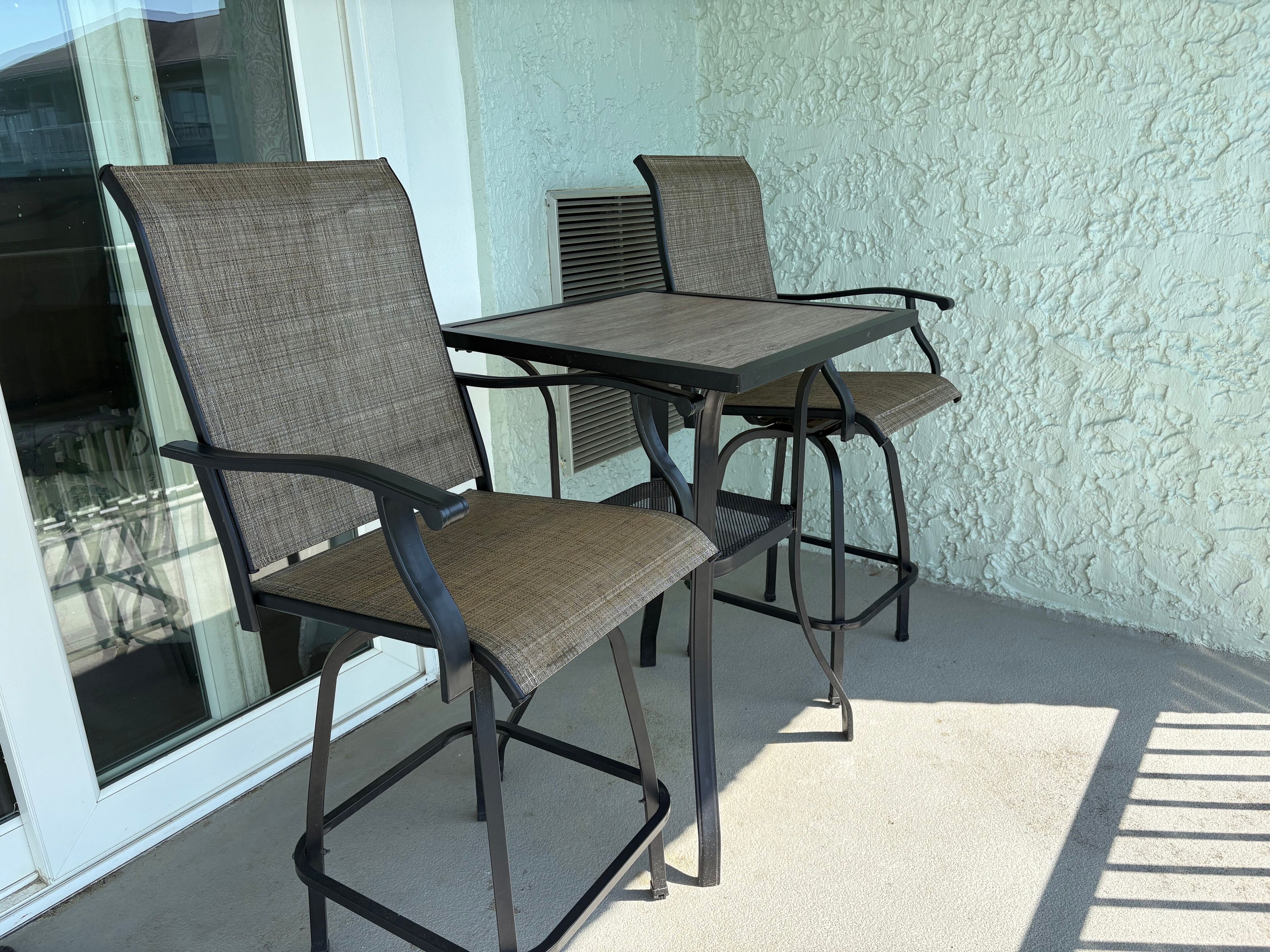 A set of four chairs and a table on a balcony with a textured wall and a window.