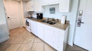 Una cocina con gabinetes blancos, encimera de granito, un lavamanos, estufa y microondas.