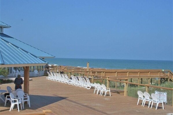 A beachside deck with white plastic chairs and a wooden railing overlooking the ocean.