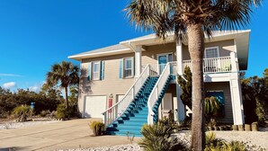 Une maison à deux étages avec un escalier bleu, une véranda et un palmier.