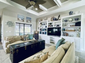 Relax in this stylish living room with a high ceiling, beige sofa, and nautical-themed artwork.