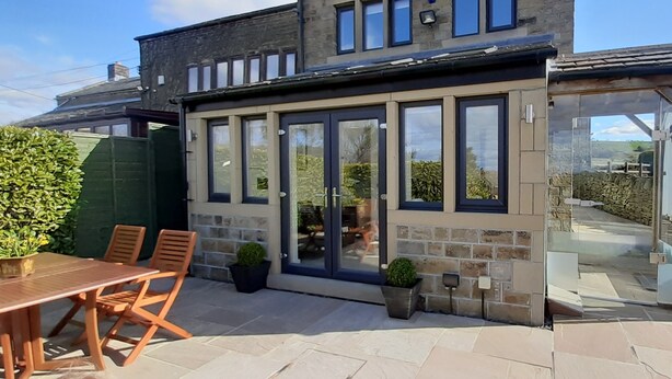 A modern house with a glass conservatory, a patio with a table and chairs, and a stone wall. - Lane End Cottage Holmfirth - Panoramic Views, Modernised with offroad parking  (Snowgate Head)