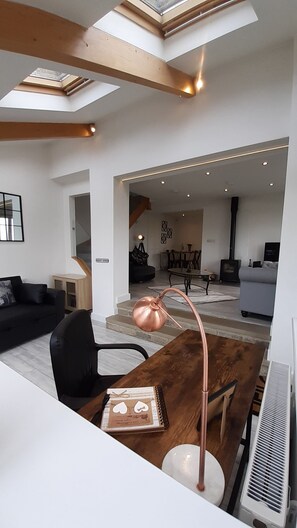 A modern living room with a wooden dining table, a black sofa, and a ceiling skylight.