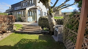 A house with a stone staircase leading to a glass door, surrounded by a well-maintained lawn and a wooden fence. - Lane End Cottage Holmfirth - Panoramic Views, Modernised with offroad parking  (Snowgate Head)