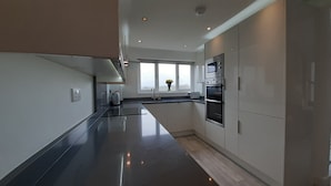 A modern kitchen with a sleek design, featuring stainless steel appliances, a black countertop, and a window with a view of the outdoors. - Lane End Cottage Holmfirth - Panoramic Views, Modernised with offroad parking  (Snowgate Head)