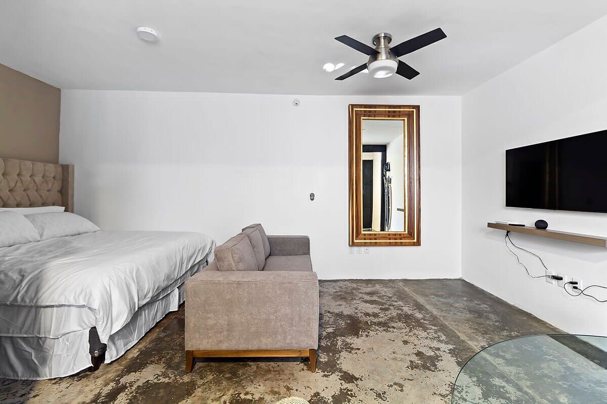 Une chambre à coucher avec un lit, un canapé, un ventilateur de plafond, une télévision et un miroir.