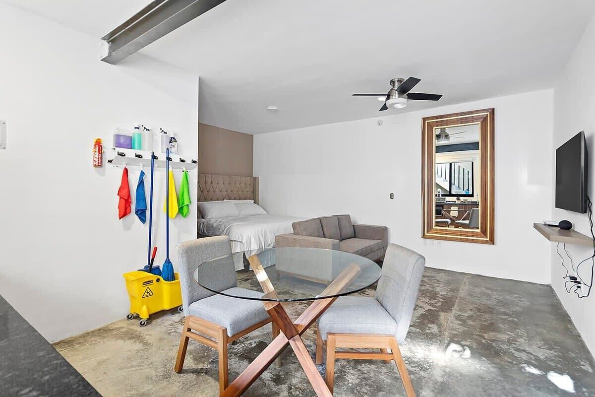 Ein modernes Wohnzimmer mit einem Glastisch, grauen Sofas, einem Deckenventilator, einem wandmontierten Fernseher und einem Gemälde an der Wand.