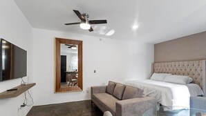 A modern hotel room with a bed, a sofa, a glass coffee table, a TV on a shelf, and a ceiling fan. - +MS +Loft Extraordinario  +Cómodo +Internet (Santiago de Querétaro)