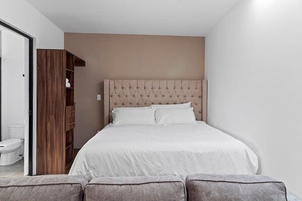 A bedroom with a large bed, a wooden wardrobe, and a toilet visible through an open door.