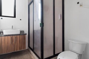 A bathroom with a white sink, wooden cabinets, a glass shower enclosure, and a white toilet.