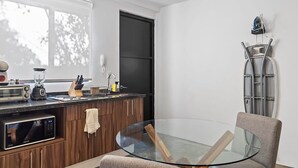 A modern kitchen with a glass table and a chair, a microwave, a toaster, and a blender on the counter. - +MS +Loft Céntrico +Cómodo +Internet (Santiago de Querétaro)